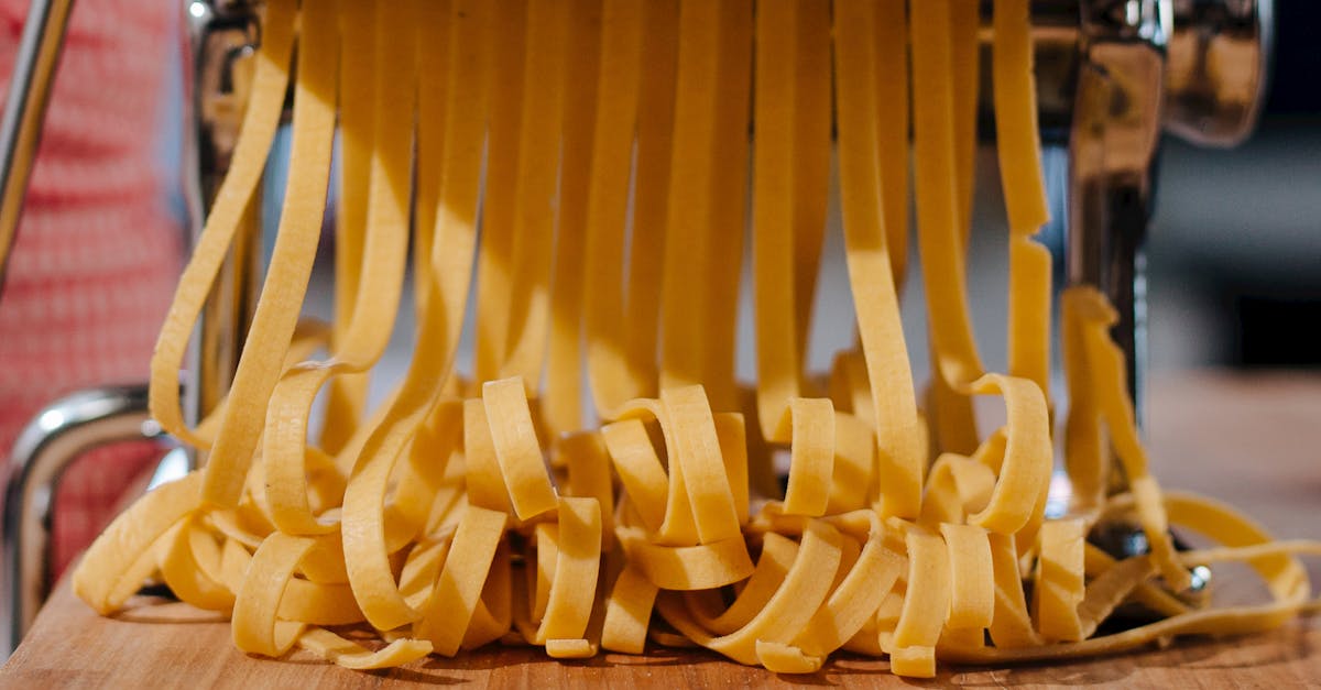 Close-up of fresh pasta strands being made with a pasta machine in an indoor kitchen setting.