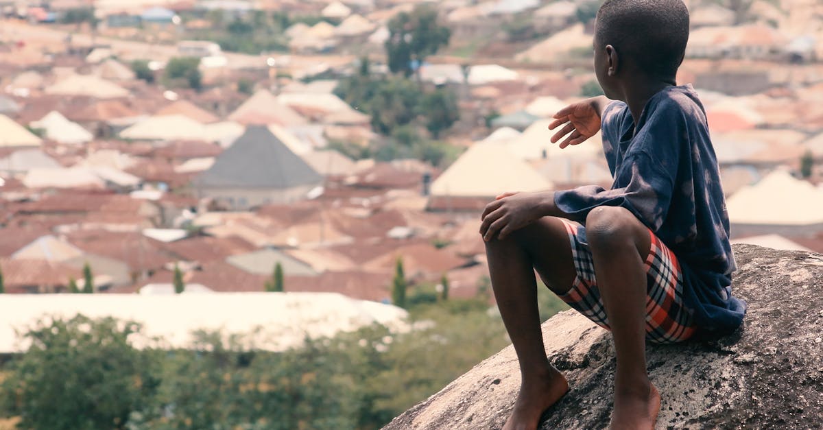 Young boy sits on a rock, overlooking a sprawling cityscape. Serene moment captured.