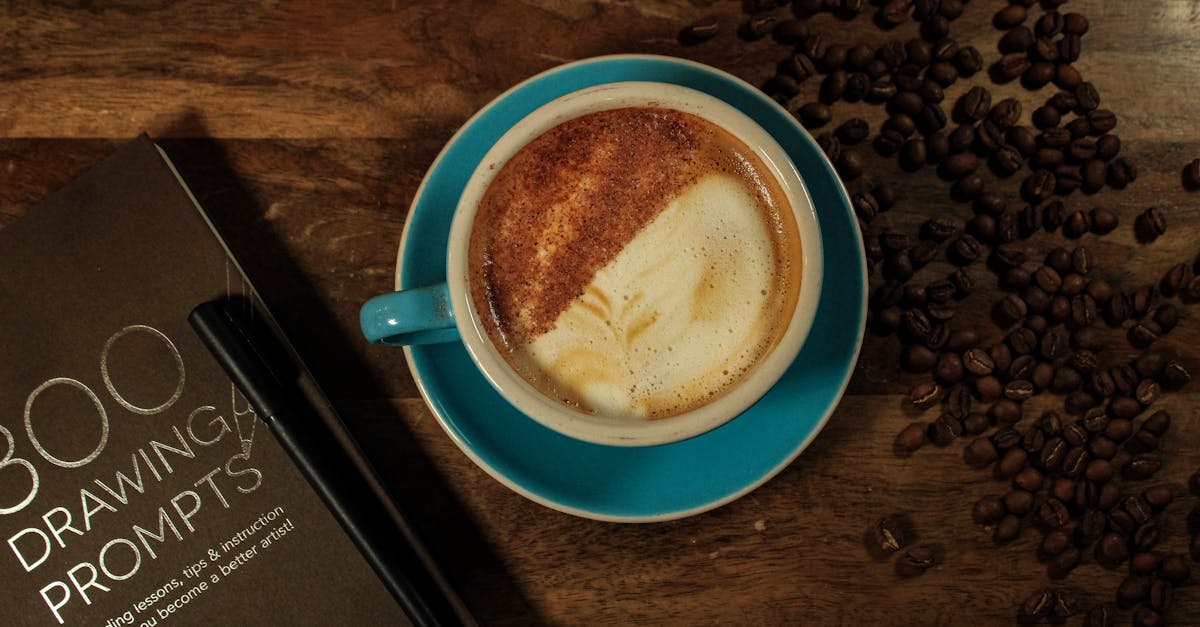 Top view of a latte with coffee art, beans, and a sketchbook on a wooden table.