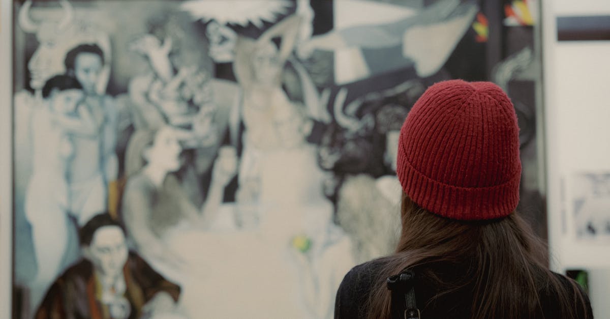 A woman in a red knit hat observes a painting in an art gallery, admiring the abstract work.