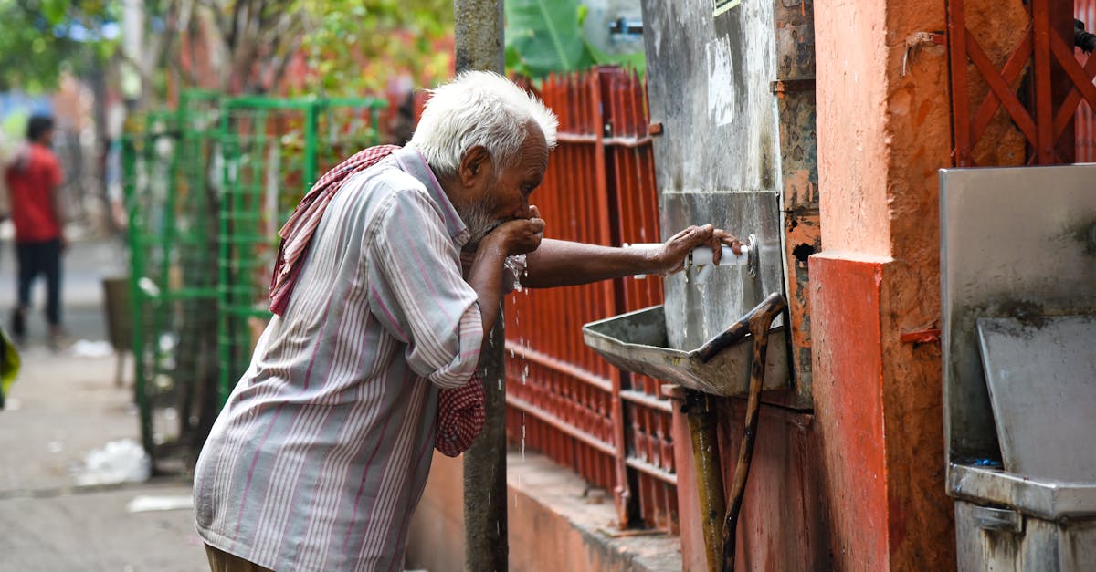 Senior man hydrating at a street water fountain, urban outdoor shot.