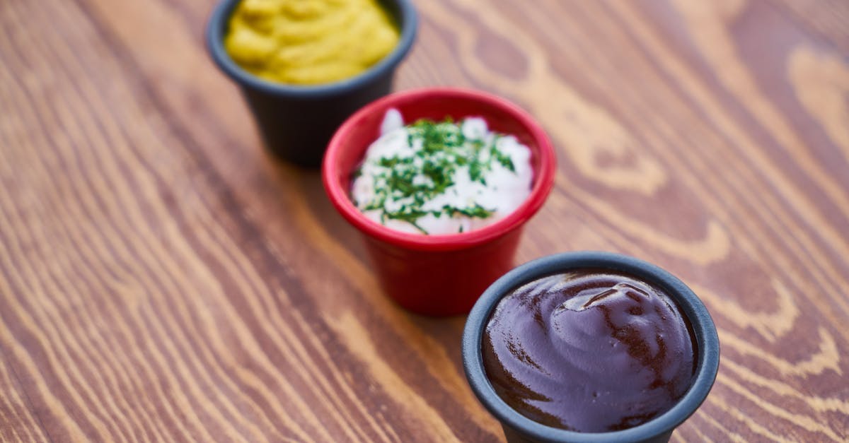 A close-up of three sauces in cups on a wooden surface, arranged in line.