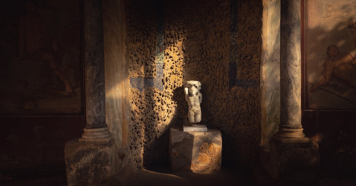 A sunlit ancient stone statue surrounded by columns and murals in a museum corridor.