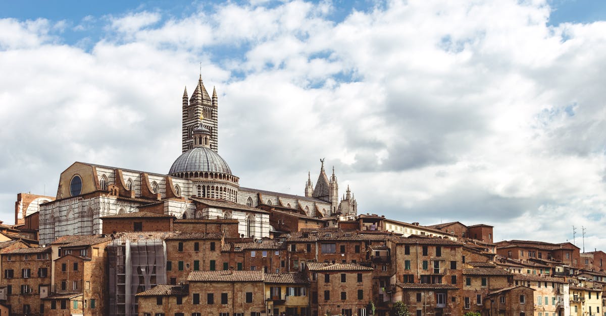 A scenic view of Siena's historic cityscape featuring the iconic Siena Cathedral under a cloudy sky in Tuscany, Italy.