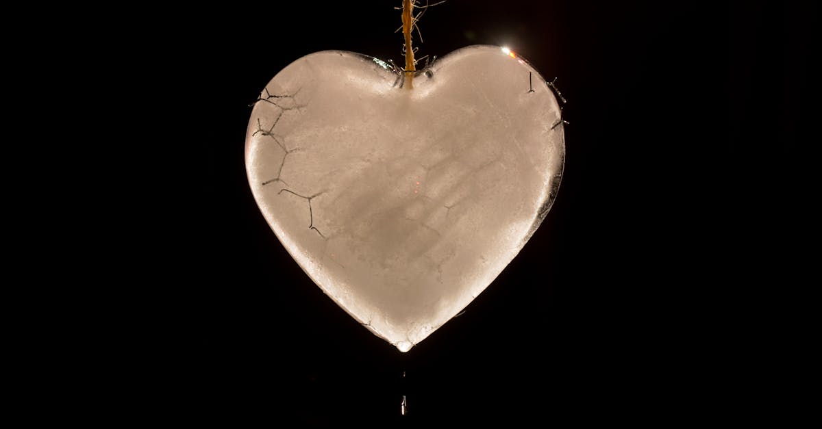 A cracked heart-shaped ice sculpture hanging by a string in darkness.