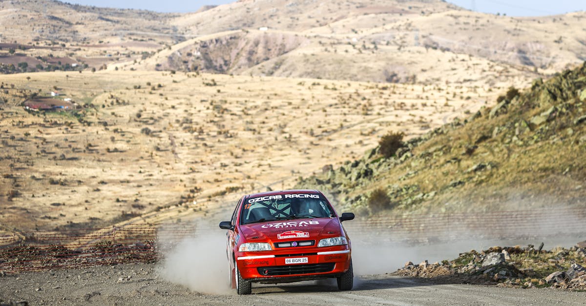 Red rally car speeding through a dusty desert landscape, leaving a trail of dust behind.