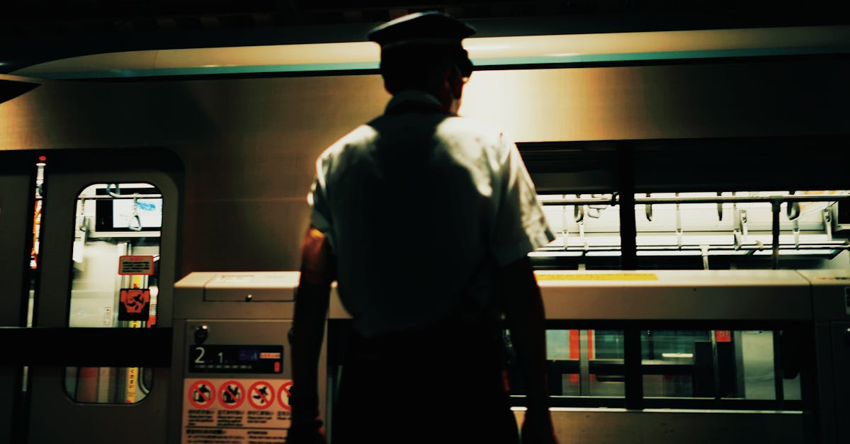 Silhouetted station worker at a subway platform during night, overseeing train arrival.