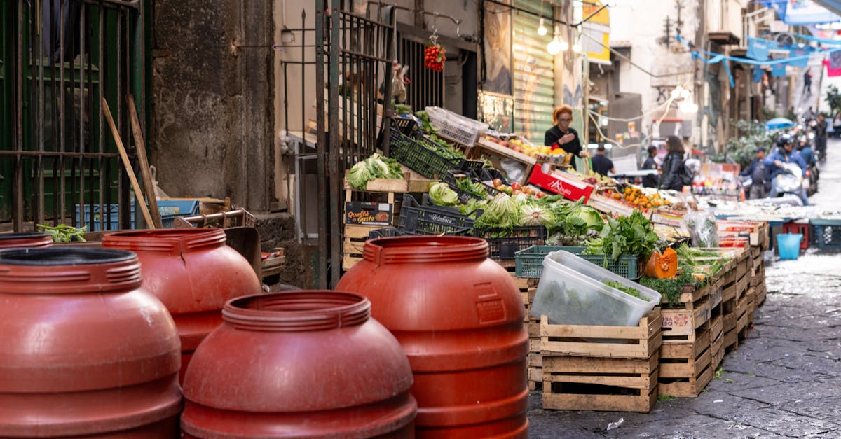 A lively urban market street scene with fresh produce and red barrels displaying local culture.