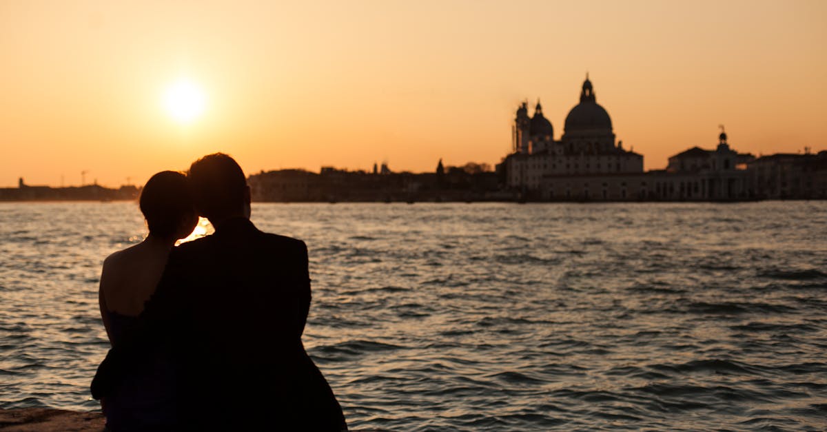 Couple silhouetted at sunset overlooking Venetian water and skyline.