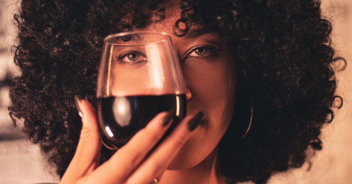 A woman with curly hair enjoys a glass of red wine, exuding elegance and celebration.