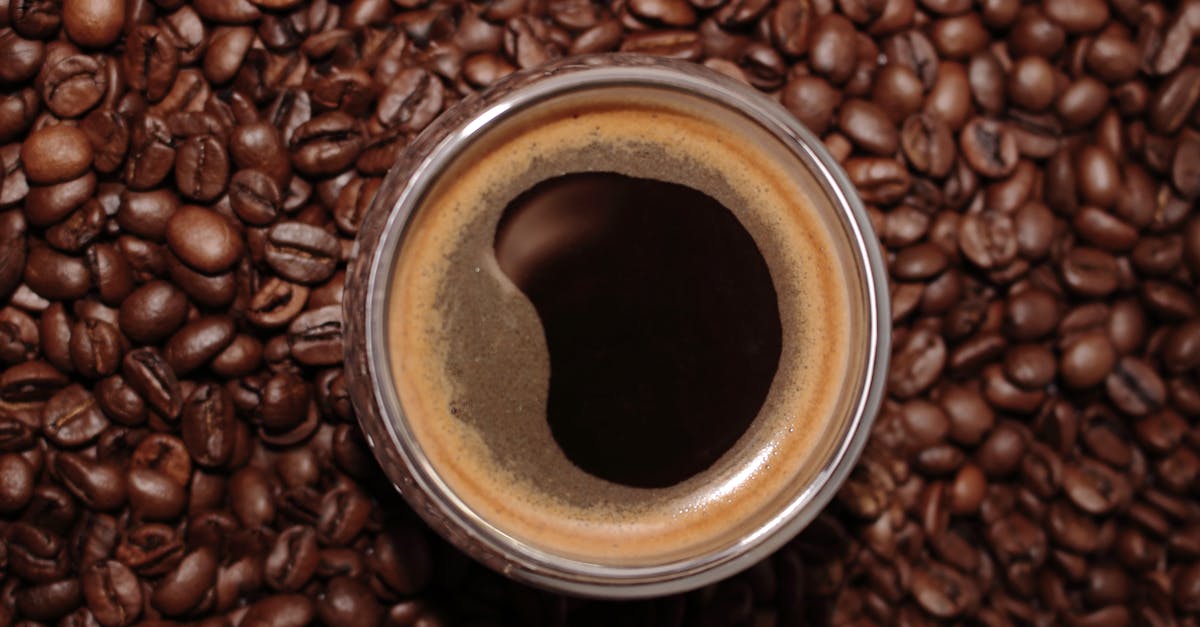 A close-up top view of an espresso cup surrounded by roasted coffee beans.