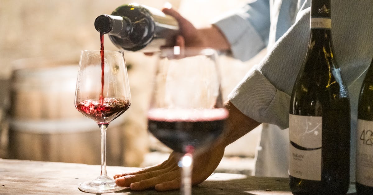 A person pouring red wine into a glass in a rustic, cozy wine bar setting.