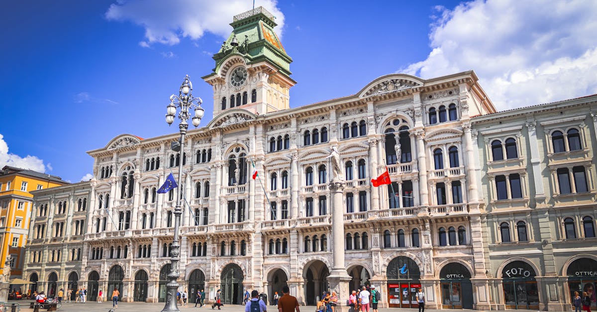 Daytime shot of Trieste City Hall's elegant architecture in Italy with people and flags displayed.