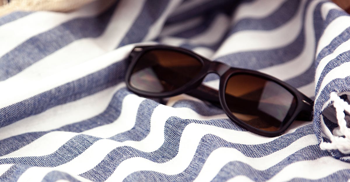 Close-up of stylish black sunglasses on a striped blue and white beach towel, perfect for summer leisure.