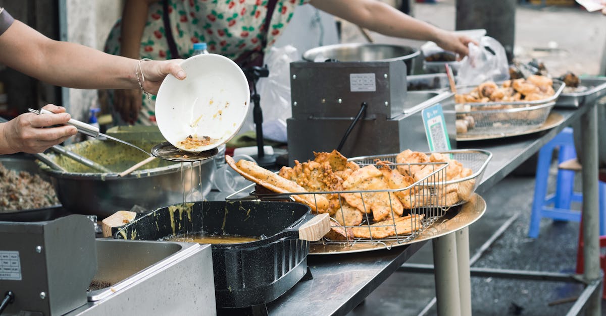 Street food stall with hands preparing fried dishes, showcasing vibrant market life.