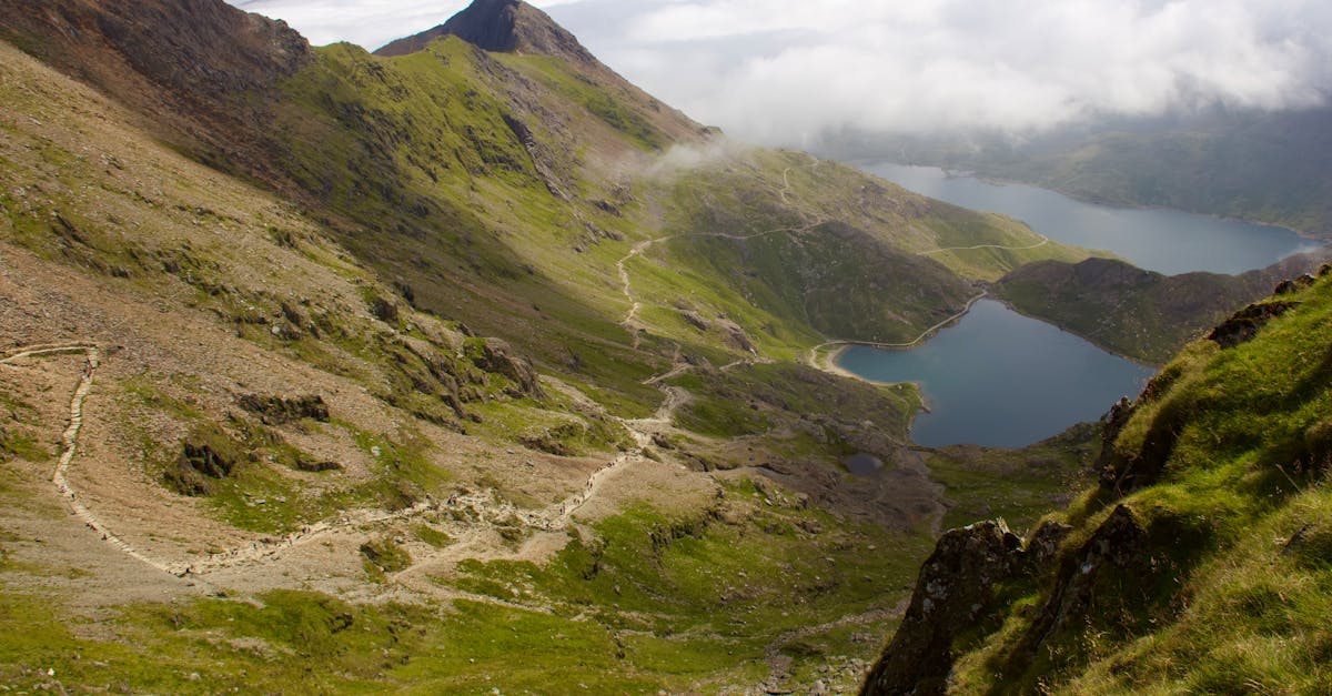 A breathtaking view of a winding mountain path with tranquil lakes and misty peaks.
