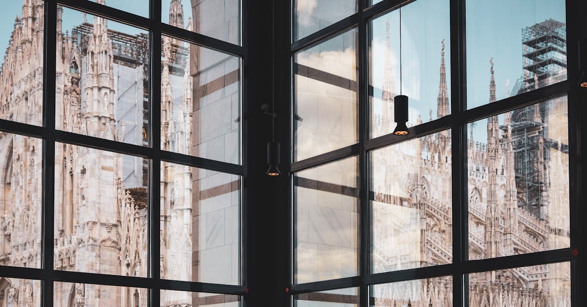 The intricate facade of Duomo di Milano reflected in a building's glass windows, showcasing Gothic architecture.