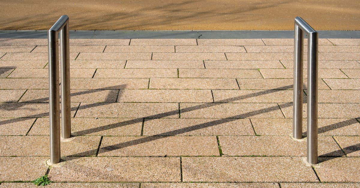 A clean, empty bicycle stand on a textured paved sidewalk with shadows, street in sight.