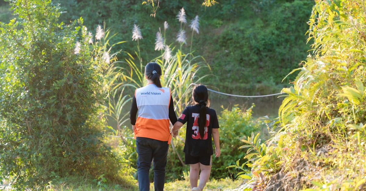 A volunteer and a child walking hand-in-hand along a scenic nature path on a sunny day.
