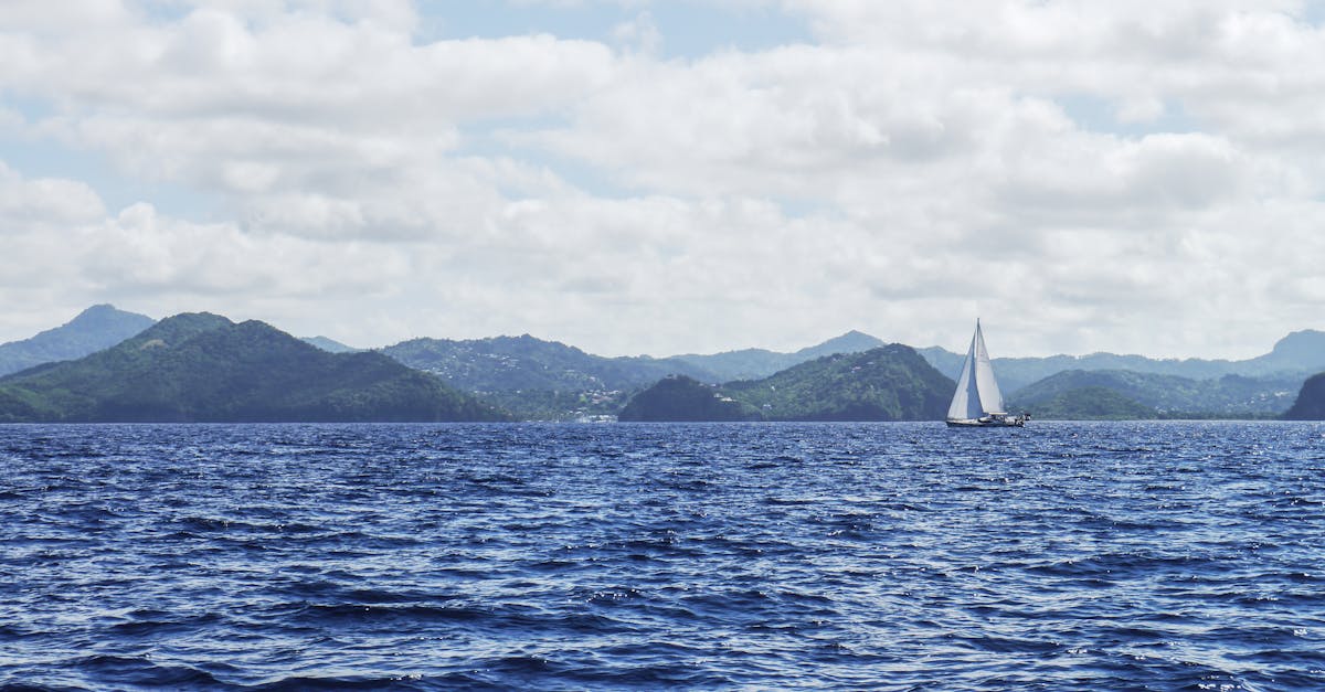 Sailboat gliding across the vast blue sea with distant green islands under a clear sky.