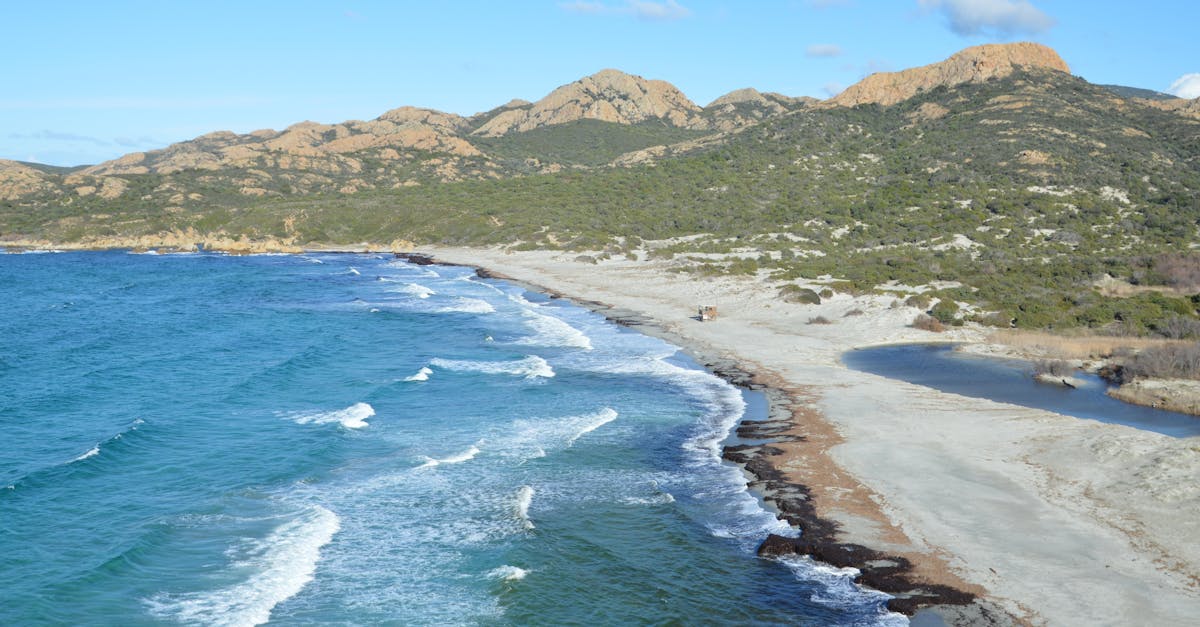 A stunning coastal view with turquoise waves meeting sandy shores and mountains in Corsica, France.