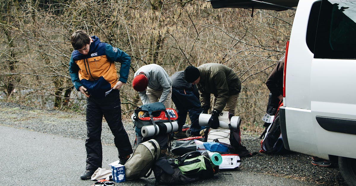 A group of travelers prepares their gear for an outdoor hiking adventure by their vehicle on a scenic road.