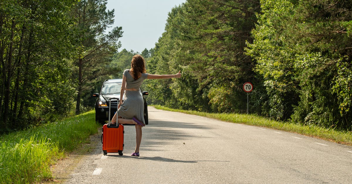 A woman hitchhiking with an orange suitcase on a rural road in Estonia during summer.