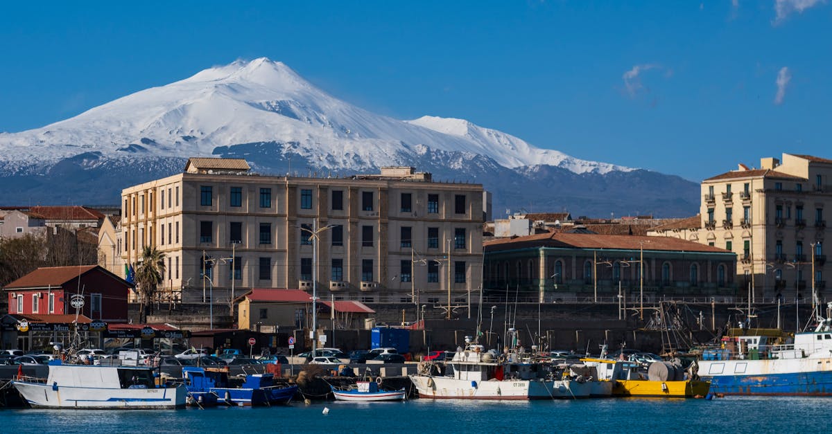 View of Mount Etna with snowy peaks over Catania's vibrant harbor in Sicily, Italy.