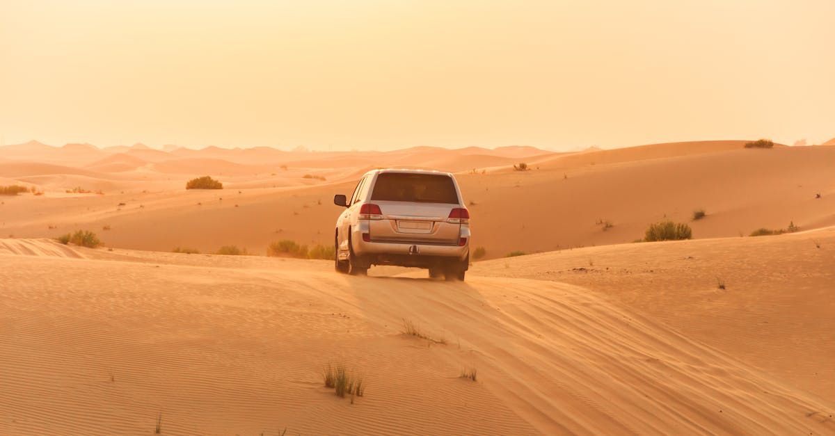 A white SUV driving through the sand dunes of the Arabian desert at sunset, capturing adventure and solitude.
