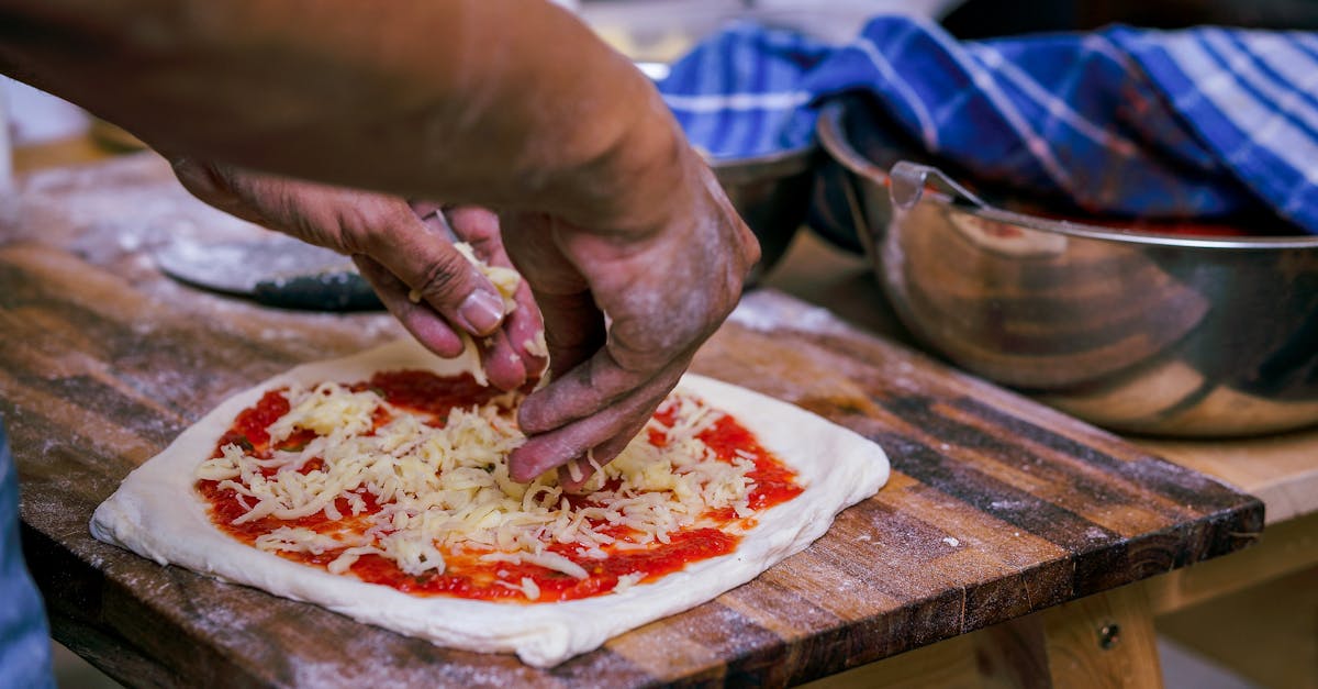 Close-up of a person adding cheese to a homemade pizza on a wooden board.