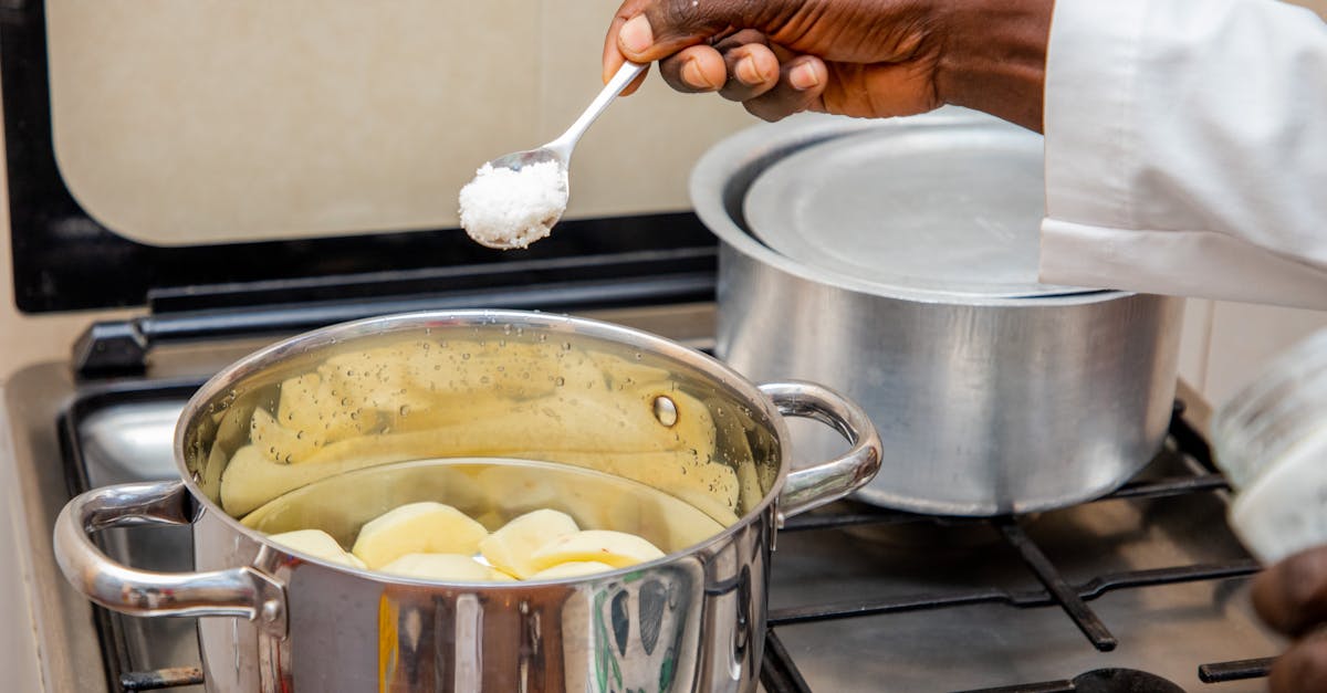 Close-up of a cook adding salt to a pot of boiling potatoes on a stove in Bujumbura, Burundi.