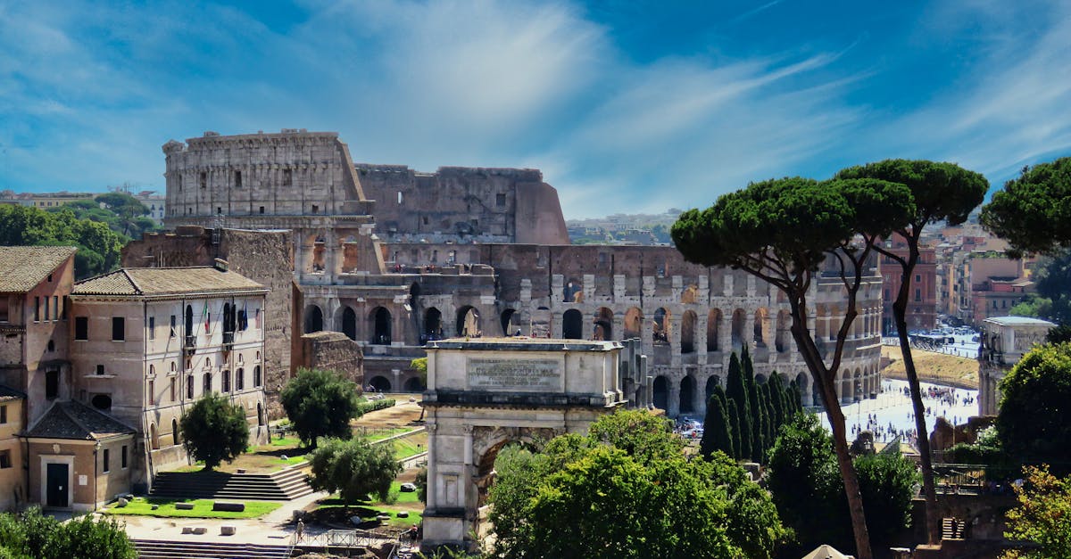 From above of aged masonry Colosseum and ancient arch near trees under bright blue cloudy sky in Italy