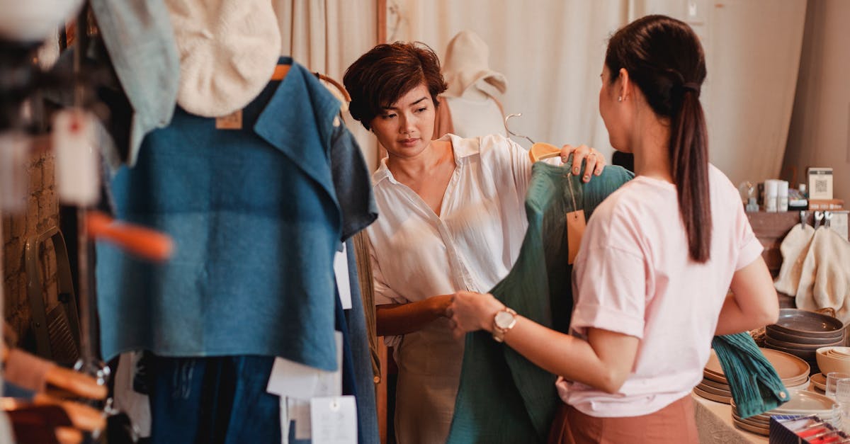 Anonymous female buyer with attentive ethnic friend choosing blouse in clothing store while spending time together on weekend