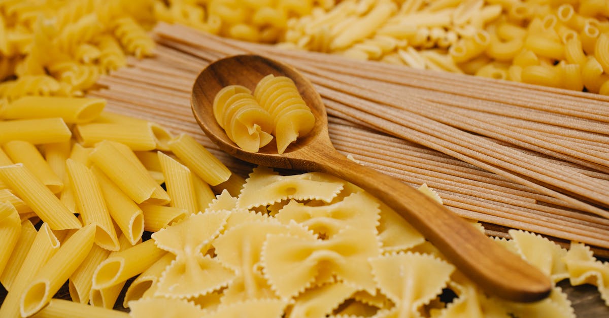 From above of various types of uncooked pasta including spaghetti penne and farfalle with wooden spoon