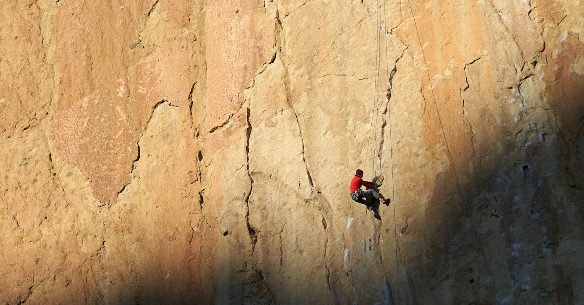 A rock climber in red scaling a steep cliff face during daylight, highlighting extreme sports adventure.