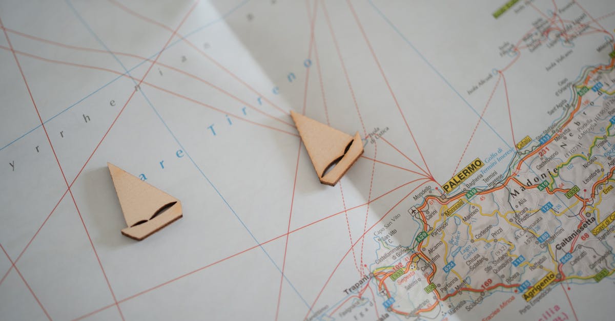 Flat lay of a nautical map with sailboat cutouts representing travel planning to Sicily.