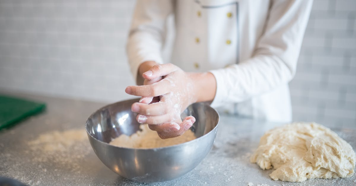 A person kneads dough in a modern kitchen with stainless steel and flour.