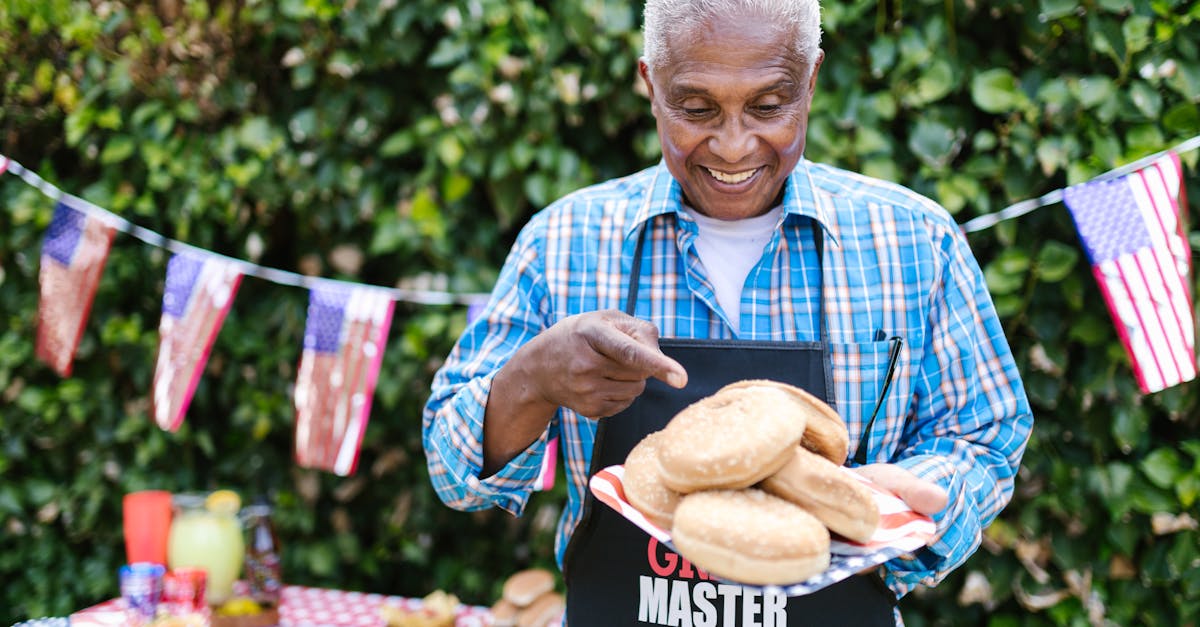Elderly man in apron holding burger buns at a 4th of July barbecue celebration.