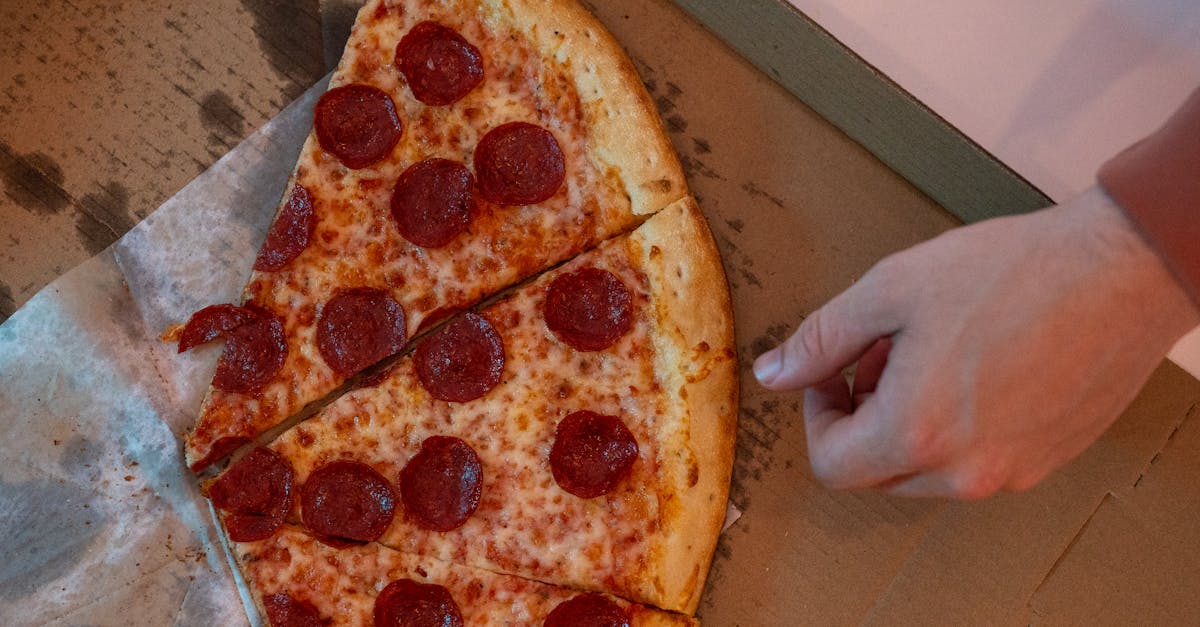 Hand reaching for a delicious pepperoni pizza slice in a cardboard box.