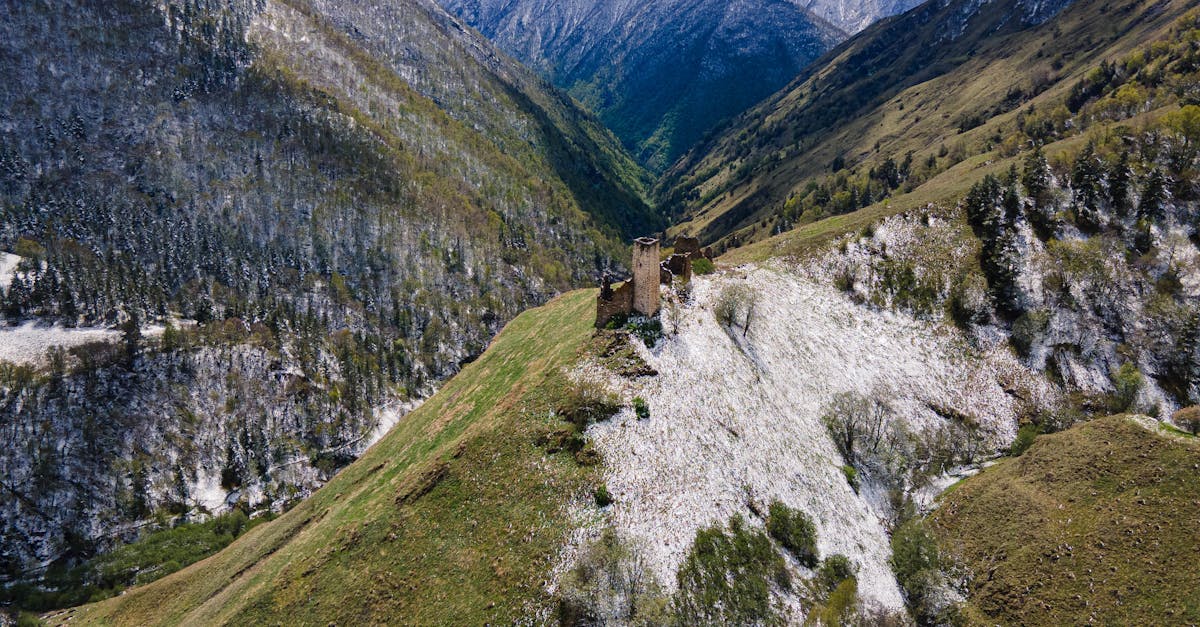 Stunning aerial view of snow-dusted mountains and ancient ruins in a lush valley.
