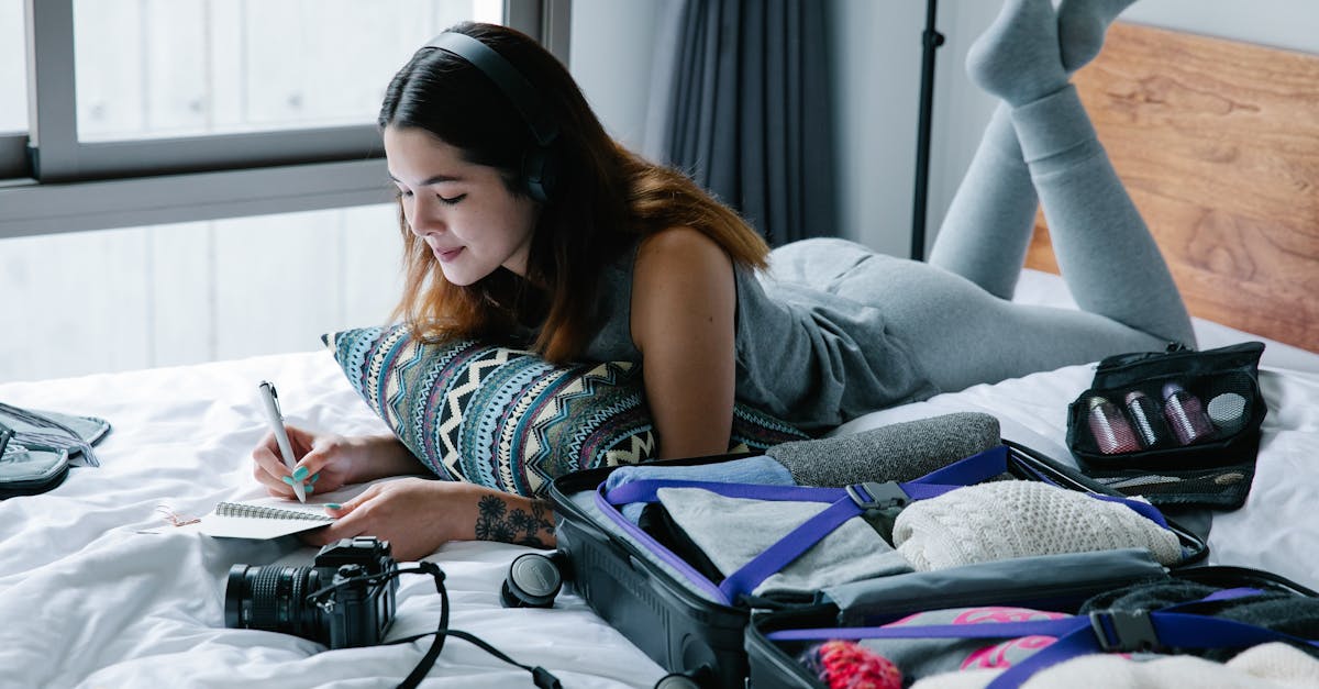 Woman lying on bed with headphones, writing in notebook, and packing suitcase.