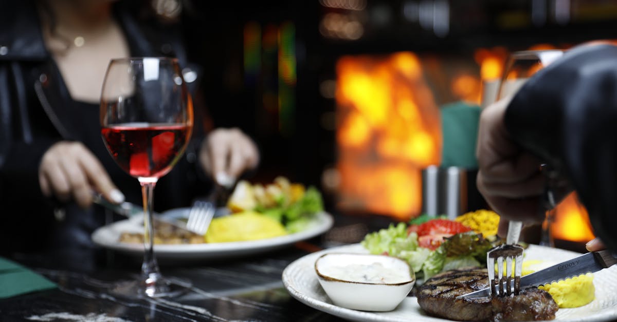 Couple enjoying a cozy dinner with steak and red wine in a warm, intimate setting.